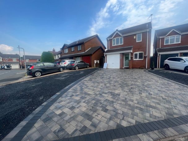 Block Paving Residential street with two houses, parked cars, and a clear blue sky.