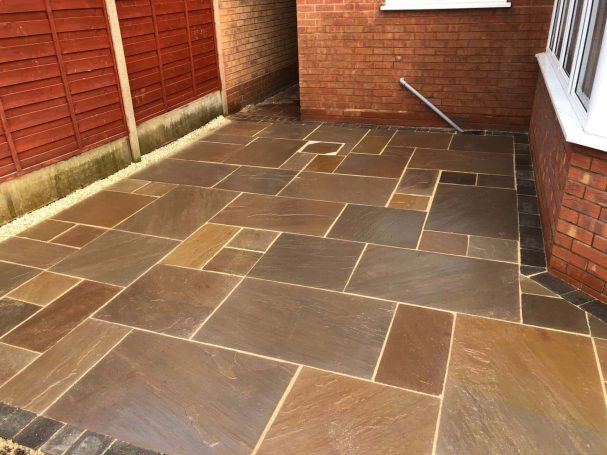 Natural Stone Paved patio area with varied stone colours and a red brick wall backdrop.