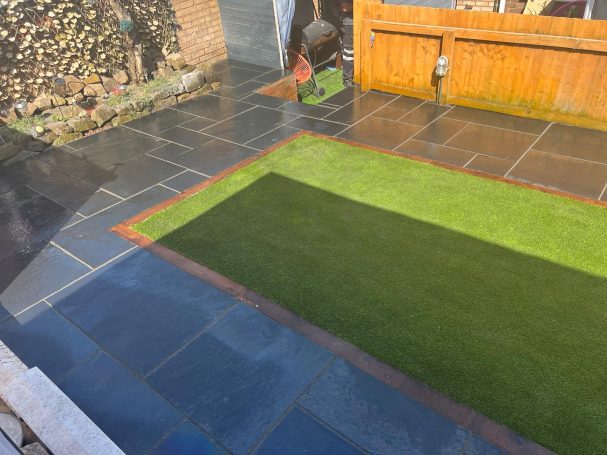 Landscaping A patio with stone tiles, a small patch of artificial grass, and wooden fencing.