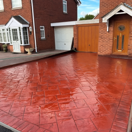 Imprinted Concrete Red stamped concrete driveway with a side garage and wooden door.
